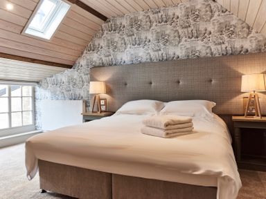 A bedroom with a bed with folded towels a skylight window and bedside lamps at The Clocktower in Humshaugh