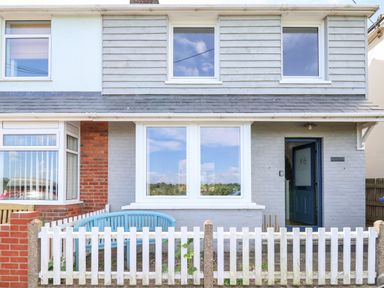 Front view of a two-story house with white picket fence blue bench and an open blue door at Long View in Southwold