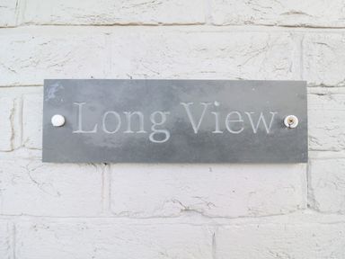 A metal sign with the words Long View mounted on a white brick wall at Long View in Southwold