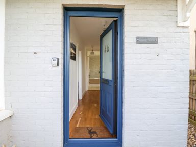 An open blue front door with number 46 leading to a hallway with wooden floor at Long View in Southwold