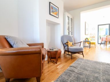 A living room with a brown leather armchair a blue upholstered chair and a small wooden table at Long View in Southwold