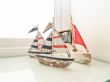 Three small wooden model sailboats on a glass surface near a window with white walls at Long View in Southwold