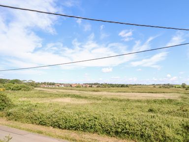 A rural landscape with fields shrubs and distant houses under a blue sky with clouds at Long View in Southwold