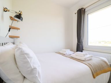 A bedroom with a bed made with white linens towels on the bed and a window with dark curtains at Long View in Southwold