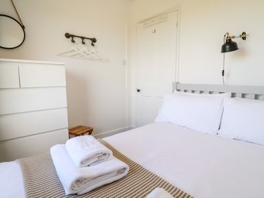 A bedroom with a bed with white linens and stacked towels on a blanket next to a white dresser and a closed door at Long View in Southwold