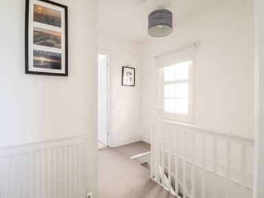 A hallway with a staircase window framed pictures and a radiator at Long View in Southwold