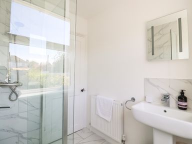 A bathroom with a glass shower enclosure a white sink a radiator with a towel and a mirror cabinet at Long View in Southwold