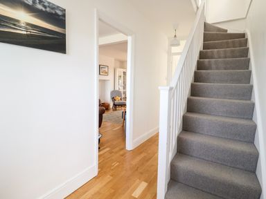 A hallway with carpeted stairs and hardwood floor leading to a living room at Long View in Southwold
