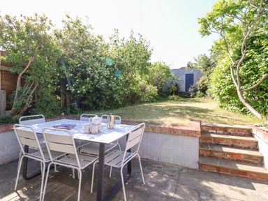 A patio with a table and chairs set with teapot and mugs overlooking a small garden with steps at Long View Southwold