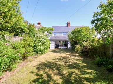 A garden with grass and bushes leading to a house with sliding glass doors at Long View in Southwold