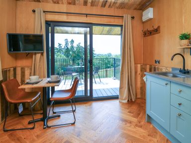 A kitchen area with a small dining table and two chairs next to sliding glass doors leading to a balcony at Hen's Hideaway in Rhaedr Gwy near Rhayader