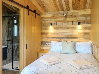 A bedroom with a bed next to a wooden sliding door leading to a bathroom at Hen's Hideaway in Rhaedr Gwy near Rhayader