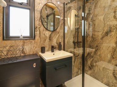 A bathroom with a sink vanity and shower enclosure with a glass door at Hens Hideaway in Rhaedr Gwy near Rhayader