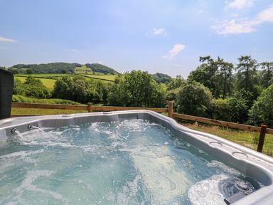 An outdoor hot tub with bubbling water overlooking green fields and trees at Hens Hideaway in Rhaedr Gwy near Rhayader