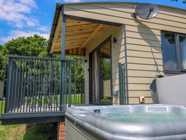 A hot tub next to a small covered porch with a table and chairs at Hens Hideaway in Rhaedr Gwy near Rhayader