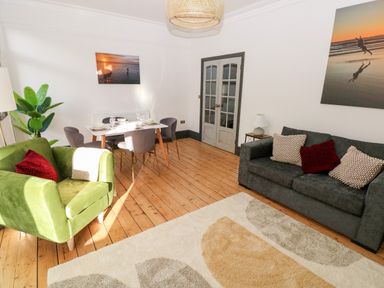 A living room with a green armchair, a gray sofa, a dining table with chairs, wooden floor and wall art at 36A Mary Street in Porthcawl