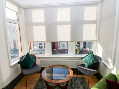 A sitting area with two chairs with green pillows and a round glass-top table near large windows at 36A Mary Street in Porthcawl