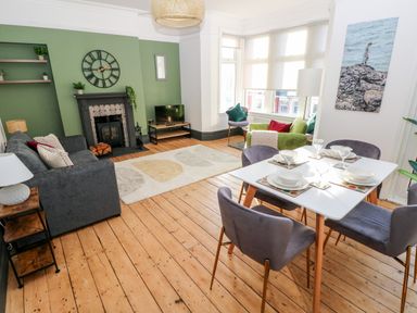 A living and dining room with a green feature wall fireplace grey sofa dining table with four chairs and large windows at 36A Mary Street in Porthcawl