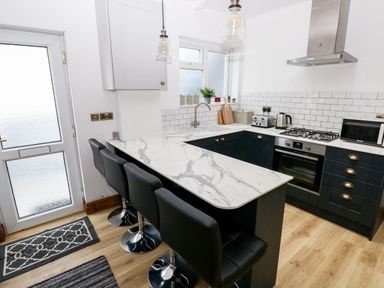 A kitchen with a marble countertop island and black chairs at 36A Mary Street in Porthcawl
