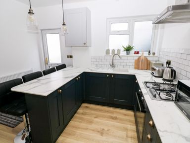 A kitchen with marble countertops dark cabinets bar stools gas stove and white tiled backsplash at 36A Mary Street in Porthcawl