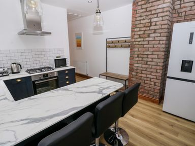 A kitchen with a marble countertop island with black chairs a brick column and a refrigerator at 36A Mary Street in Porthcawl