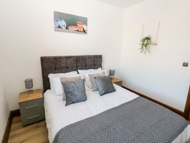 A bedroom with a double bed with grey headboard and pillows two bedside tables with lamps and a picture of boats on the wall at 36A Mary Street in Porthcawl