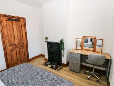 A bedroom with a wooden door a small black fireplace a desk with a tri fold mirror and a gray office chair at 36A Mary Street in Porthcawl
