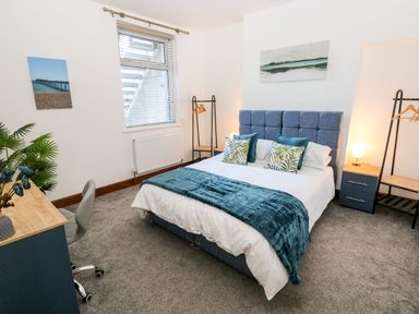 A bedroom with a bed a desk chair plants and wall art at 36A Mary Street in Porthcawl