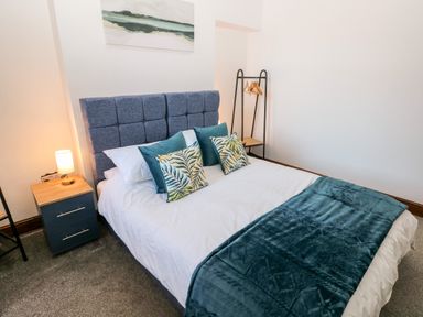 A bedroom with a bed a blue headboard a bedside table with a lamp and a clothing rack at 36A Mary Street in Porthcawl