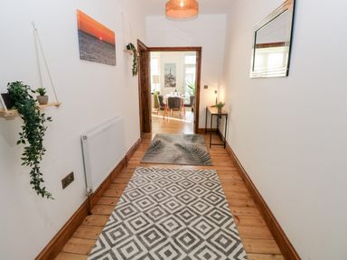 A hallway with rugs on a wooden floor plants on shelves and a view into a dining room at 36A Mary Street in Porthcawl