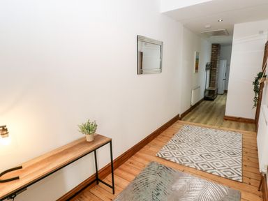 A hallway with wooden floor and two rugs a narrow wooden table with a lamp and small plant and a mirror on the wall at 36A Mary Street in Porthcawl