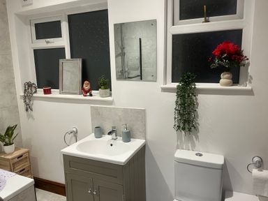A bathroom with a sink, toilet, bathtub, plants, and decorative items on window sills at 36A Mary Street in Porthcawl