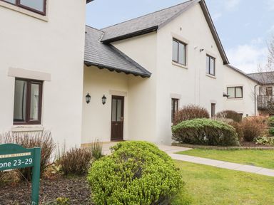 A white two-story house with a dark brown door and windows with bushes and a walkway in front at Whitbarrow 24 in Penruddock