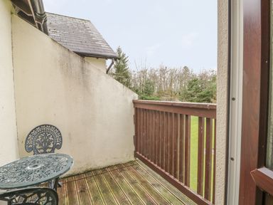 A small wooden balcony with a metal table and chairs overlooking a grassy area and trees at Whitbarrow 24 in Penruddock