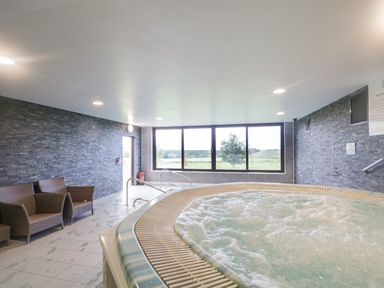 An indoor pool area with a hot tub and wicker chairs next to large windows showing an outdoor view at Whitbarrow 24 in Penruddock