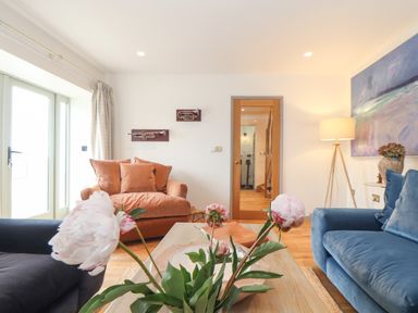 A living room with a blue sofa a brown armchair flowers on a coffee table and musical instrument wall decorations at The Riblows Cape Cornwall in Bollowal near St Just