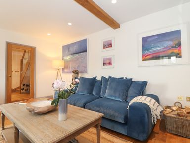 A living room with a blue sofa a wooden coffee table with flowers a basket with logs and paintings on the wall at The Riblows Cape Cornwall Bollowal near St Just
