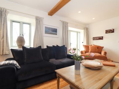A living room with black and orange sofas a wooden coffee table with a vase of flowers and wall decorations at The Riblows Cape Cornwall Bollowal near St Just