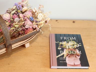 A wooden table with a basket of dried flowers and a book titled From Seed to Bloom by Milli Proust