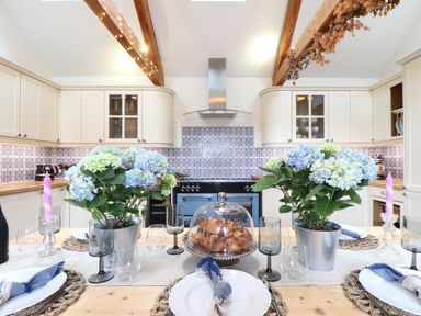 A kitchen with a wooden table set with plates glasses candles flowers and pastries at The Riblows Cape Cornwall Bollowal near St Just