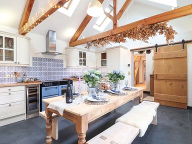 A kitchen with a wooden dining table set with plates and flowers and white cabinets with blue tile backsplash at The Riblows Cape Cornwall in Bollowal near St Just
