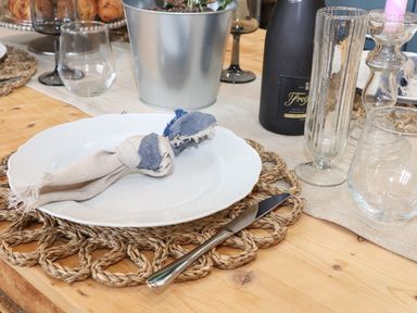 A dining table set with a white plate on a woven placemat a knotted cloth napkin a knife glasses a bottle and a metal bucket at The Riblows Cape Cornwall Bollowal near St Just