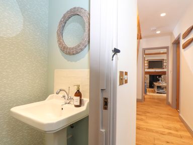 A bathroom sink with a mirror and hand wash next to a hallway leading to a living room with a fireplace at The Riblows Cape Cornwall Bollowal near St Just