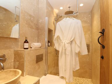 A bathroom with a sink hand wash towel and white bathrobes hanging in the shower at The Riblows Cape Cornwall