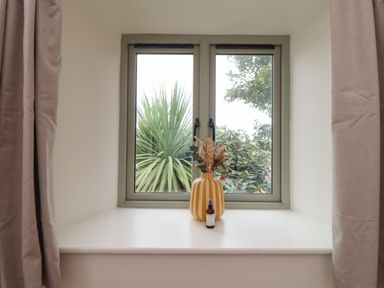 A window with green frames and closed handles with a striped vase with dried flowers and a small bottle on the windowsill at The Riblows Cape Cornwall Bollowal near St Just