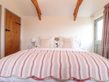 A bedroom with a bed with striped bedding pillows a wooden door bedside tables with lamps and windows with curtains at The Riblows Cape Cornwall Bollowal near St Just