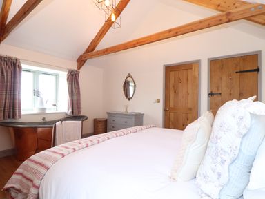 A bedroom with a bed pillows and blanket wooden doors a grey drawer a round mirror and a copper bathtub with plaid curtains at The Riblows Cape Cornwall Bollowal near St Just