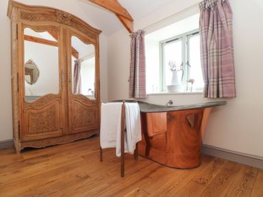 A bathroom with a copper bathtub a wooden towel rack and a carved wooden wardrobe at The Riblows Cape Cornwall