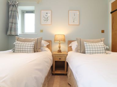 A bedroom with two single beds with cushions and a wooden nightstand with a lamp between at The Riblows Cape Cornwall Bollowal near St Just
