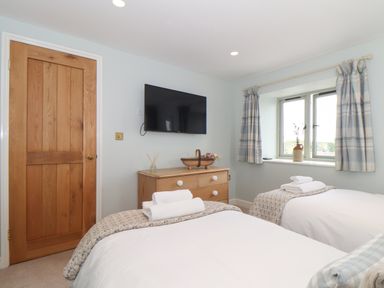 A bedroom with two single beds a wooden door a wooden chest of drawers and a television on the wall at The Riblows Cape Cornwall Bollowal near St Just